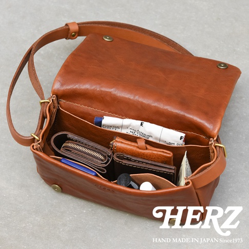 職人手作皮革Organ斜背包，駝棕色，皮革材質，包內展示有皮夾、卡夾、筆等物品。