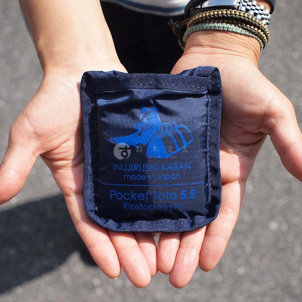 雙手捧著深藍色犬印鞄環保折疊收納購物袋，袋子表面有藍色圖案和文字，材質為 Ripstop Nylon，容量 5.5L。