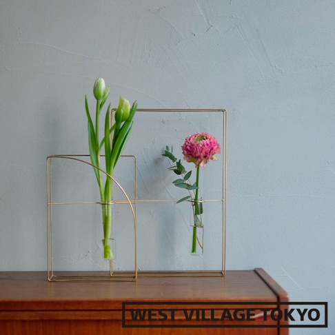 黃銅書本造型掛擺兩用花器，由金色金屬線條構成，帶有兩個獨立的玻璃試管花瓶，分別插有綠色花苞和粉紅色花朵，整體造型簡潔現代。