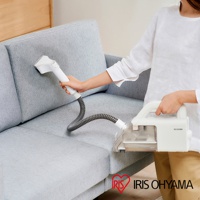 一位使用者正使用白色隨心無線織物清潔機 RNS-B200D 清潔淺灰色織物沙發。清潔機主機為白色，配有透明集塵盒，軟管為灰色螺旋狀。