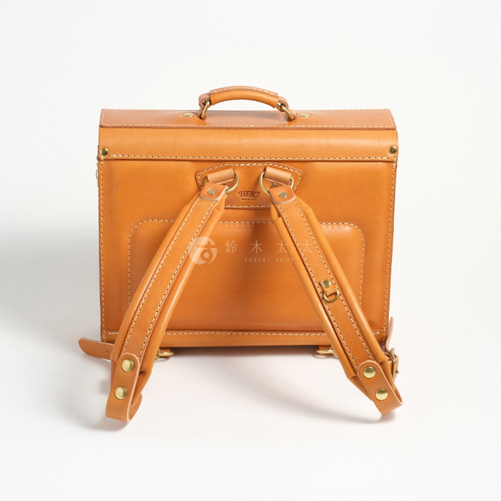 一個帶有皮革揹帶的棕褐色皮革橫式書包，書包頂部有一個提把，背面有明顯的縫線和金屬配件。