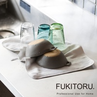 一張白色超細纖維擦拭布上，擺放著兩個灰色小碗和三個不同顏色的玻璃杯，杯子皆有水珠，整體為乾淨的廚房檯面場景。