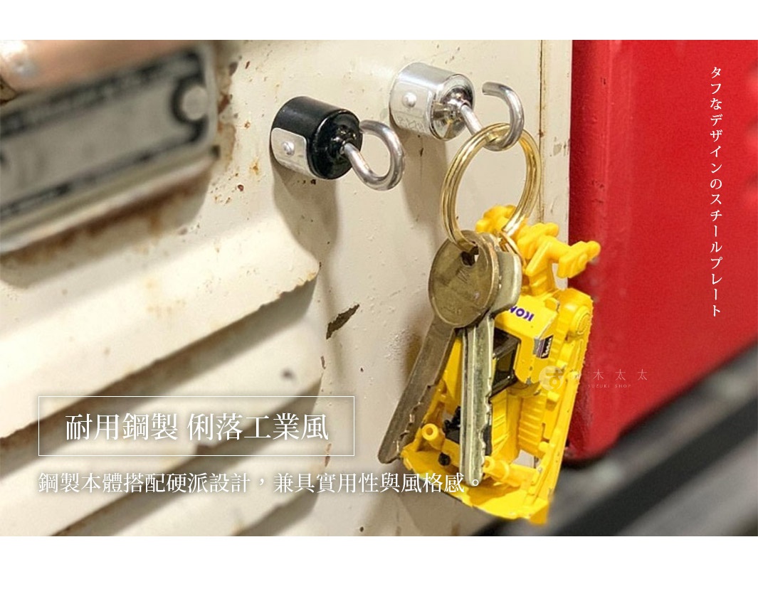 一組工業風鑰匙圈，包含兩個帶鑰匙的黃色推土機吊飾，掛在有歲月痕跡的牆壁掛勾上，背景是紅色金屬表面。