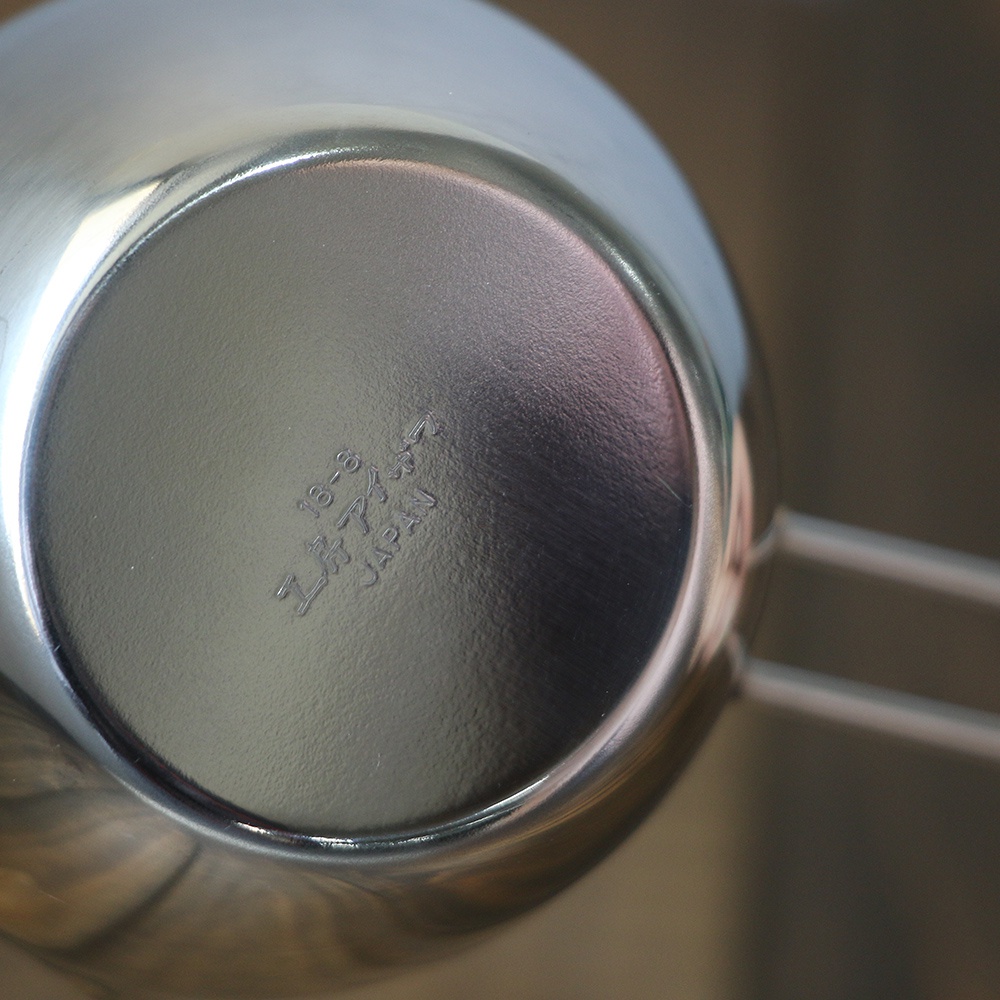 不鏽鋼長柄量杯，底部刻有「18-8 工房アイザワ JAPAN」字樣，銀色金屬材質，細節處有光澤反射。