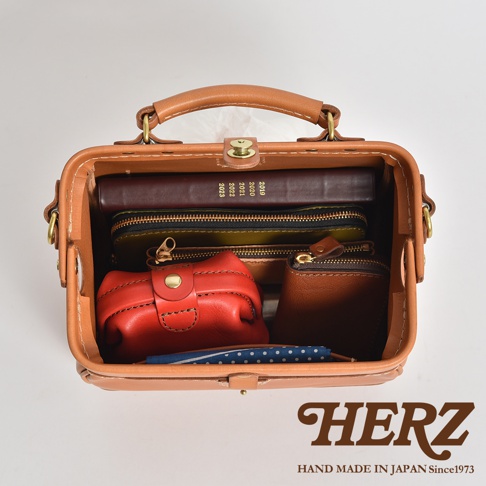 職人手作皮革口金醫生單肩包，淺棕色皮革，包內裝有紅色零錢包、綠色與棕色筆夾包、一本深棕色筆記本，以及藍色點點手帕。