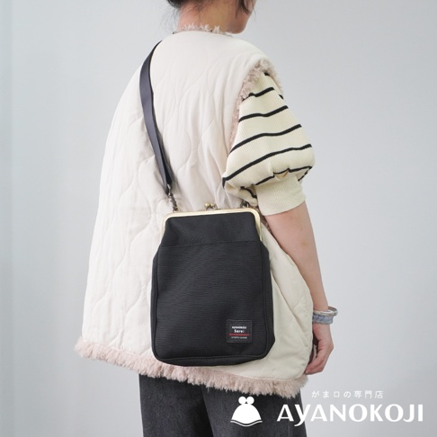 一位女性身穿白色羽絨背心和條紋袖套，斜挎一個黑色的 AYANOKOJI Sarei 口金斜背包