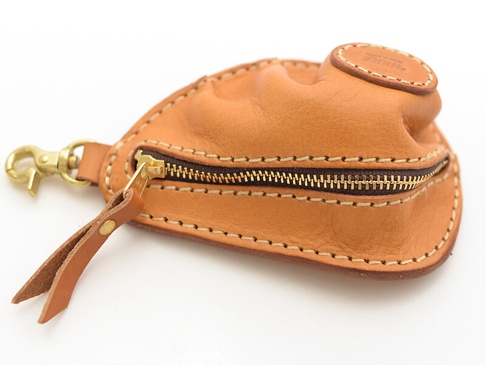 職人手作皮革餃子造型零錢包，採用淺棕色皮革製成，搭配黃銅拉鍊與掛鉤，手工縫線精緻，頂部有圓形皮革壓印標誌。