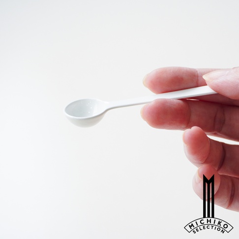 一手拿著白色琺瑯計量匙，匙面裝有少量白色粉末
