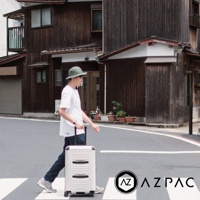一名男子推著白色 20 吋 AZPAC Trucker 旅行箱，走在日式建築前的斑馬線上。旅行箱為硬殼設計，有防爆拉鍊和兩個黑色的條紋裝飾。