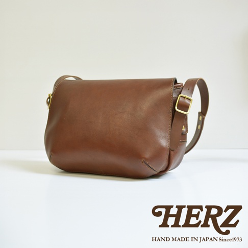 職人手作復古翻蓋郵差包，採用棕色皮革製成，配有金色金屬扣環和可調節肩帶。