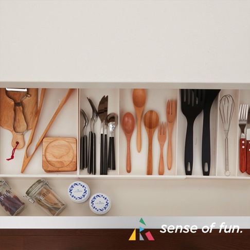 抽屜內整齊擺放著各式廚房用具，包含木質砧板、刨刀、不鏽鋼刀叉湯匙、木製湯勺、木叉、黑色鍋鏟、打蛋器，以及玻璃罐和圓形罐。