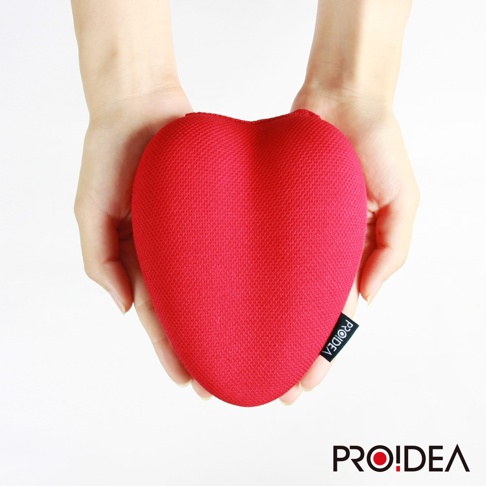 雙手捧著一個紅色愛心形狀的指壓枕，枕頭表面為網狀織物材質，一側有黑色標籤印有白色品牌名稱。