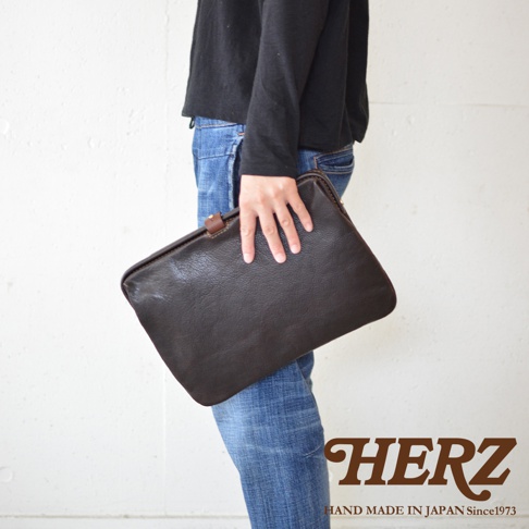 深棕色職人手作皮革Organ手拿包，簡約設計，搭配牛仔褲，展現自然質感。