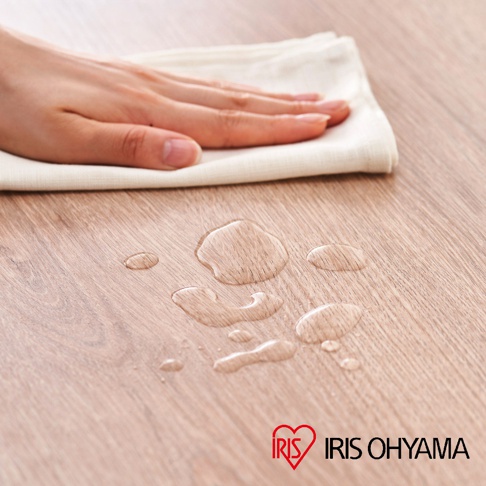 淺木紋木質桌面，表面有水漬，一隻手正用白色布擦拭。