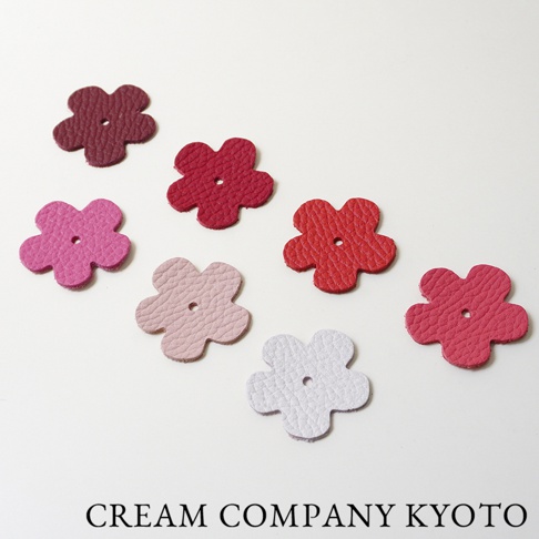 七個皮革製成的五瓣花形狀裝飾，顏色包含深紅、紅色、桃紅、粉紅和淺灰。每個花形裝飾中央都有一個小圓孔，材質呈現自然皮革紋理。