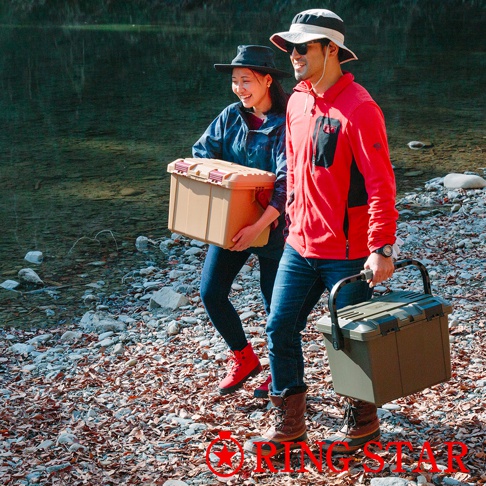 兩個人在河邊的碎石地上行走，一人手持淺棕色塑膠收納箱，另一人手持橄欖綠塑膠收納箱。