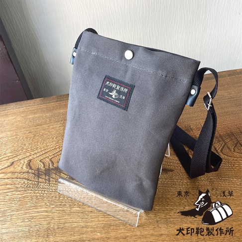 灰色帆布平板收納側背包，包身帶有品牌標籤，下方另有品牌標誌與文字。