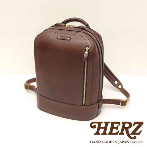 職人手作立體棕色皮革商務後背包，設有金色拉鍊和品牌標誌，皮革質感厚實，設計簡約大方。