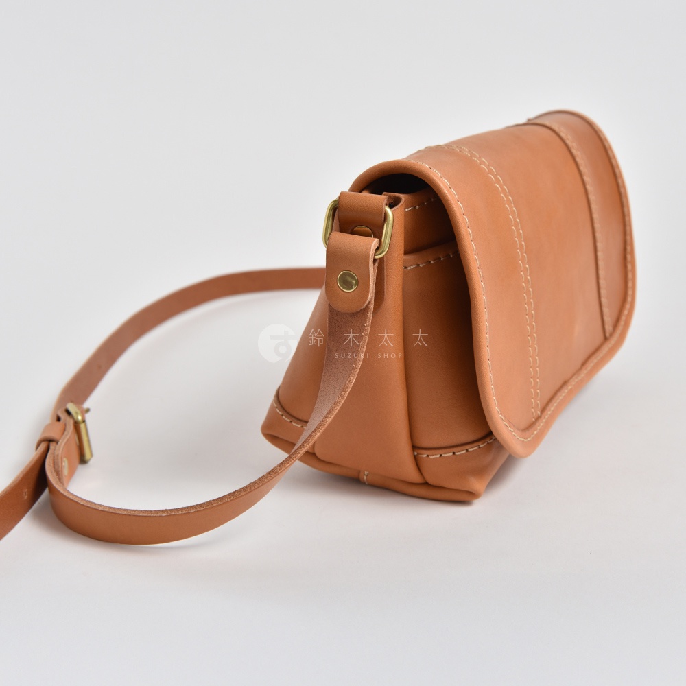 職人手作皮革復古郵差包，淺棕色，可見縫線及銅色金屬扣環，搭配可調節長度的皮革背帶。
