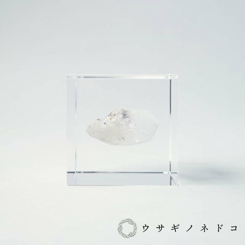 透明立方體水晶塊中，封存著一塊白色半透明的礦石，部分區域帶有淡紫色或灰色雜質，礦石表面呈現天然晶體結構。