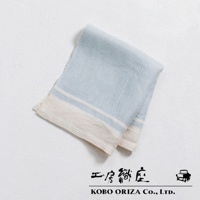 一條淺藍色純亞麻斜紋廚房拭巾，帶有米白色與淺藍色條紋邊飾，質地細緻，放在白色紋理背景上。