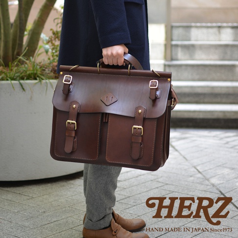 職人手作皮革旅行包 A-102，深棕色，正面有兩個翻蓋口袋，搭配金色釦環和皮帶。