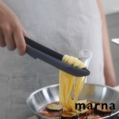 marna 標誌下方有 TOKYO 1872 文字，有人用黑色食物夾夾起正在烹煮的義大利麵，放在裝有醬汁和茄子的鍋子裡。