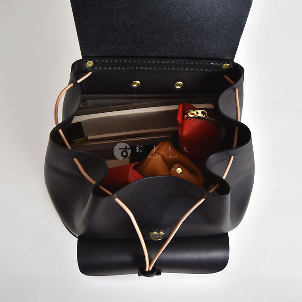 職人手作黑色皮革經典後背包，內部裝有書籍、紅色與棕色皮製小收納包，束繩與皮革抽繩設計，金屬釦具。