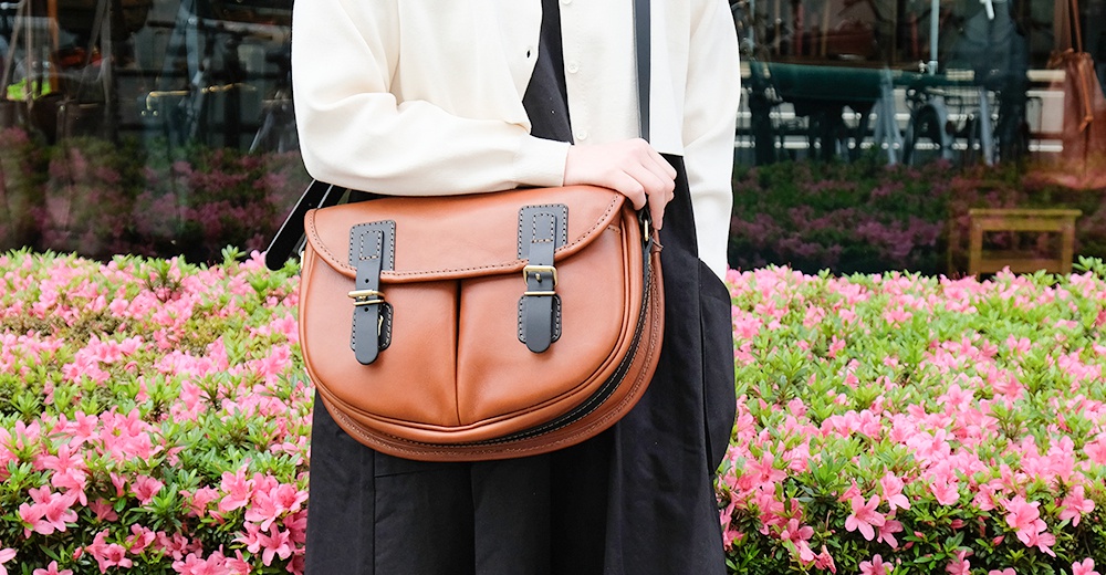 職人手作皮革傳統釣魚包，展示了栗棕色皮革包身，配有兩個黑色皮革翻蓋扣環和黃銅色搭扣。