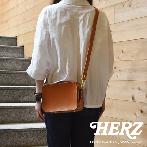 日本HERZ職人手作皮革兩用迷你小方包 CW-40 側背包，採用棕褐色硬質皮革製成，背面視角，展示包包的結構和金屬配件，下方有HERZ品牌標誌及「HAND MADE IN JAPAN Since1973」文字