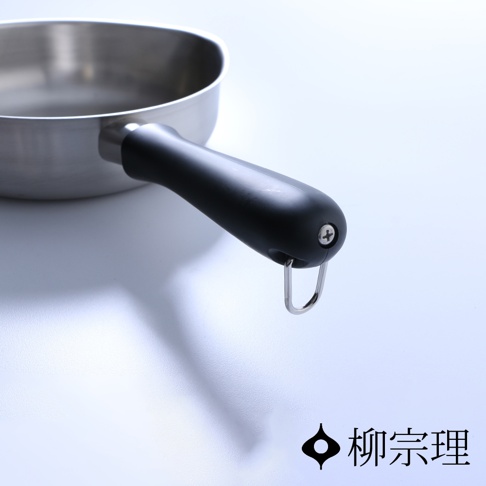 柳宗理不鏽鋼霧面單手鍋的特寫鏡頭，專注呈現黑色防燙手柄細節，柄端配有金屬掛環與螺絲固定，右下角印有柳宗理品牌標誌與文字。