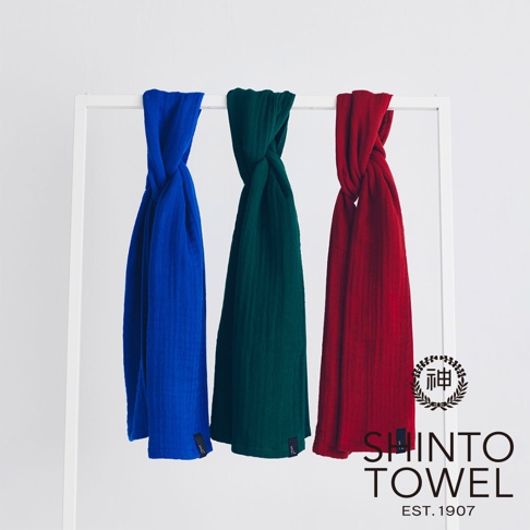 三條紋理織物，分別為亮藍色、深綠色和紅色，懸掛在白色架子上，呈現扭轉的垂墜感。