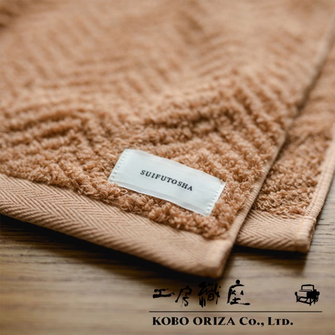 ECOR 天然系人字紋有機棉毛巾，呈現溫暖的淺棕色調，材質柔軟，帶有清晰的人字紋織法和品牌標籤「SUIFUTOSHA」。