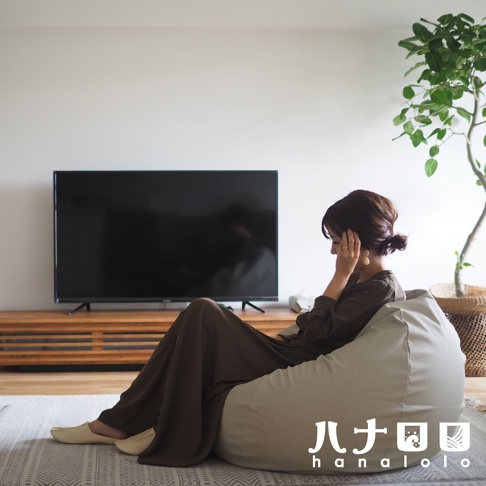 一位女士坐在淺灰色皮革款懶骨頭沙發上，沙發置於客廳地板上，背景有電視和盆栽。