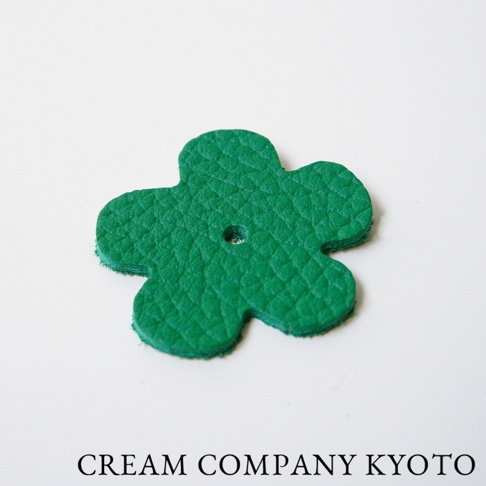 綠色皮革製作的四葉草造型吊飾，具有壓紋紋理，中央有一個小孔。