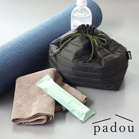 一張靜物攝影照，畫面中包含一個深灰色的 PADOU Ecorip 空氣感防潑水摺疊束口袋，束口袋旁有一條摺疊的棕色毛巾、一瓶礦泉水、一條綠色抹茶口味的能量棒，以及捲起的藍色瑜珈墊，整體營造出運動準備的氛圍，右下方則印有 padou 品牌名稱。