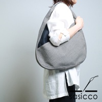 一位女士斜挎著一個三河木綿刺子織半月包，包身以黑白格紋圖案為主，一側點綴有黑色皮革拼接。