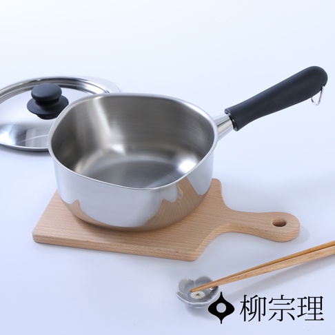 亮面不鏽鋼單手鍋，鍋身呈銀色，配有黑色防燙手柄，鍋蓋為不鏽鋼材質，帶有黑色圓形提鈕。鍋具放置於淺色木質砧板上，旁有一對木筷子放在花朵造型的淺碟中。