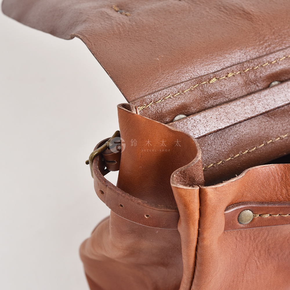 棕色皮革復古郵差包，特寫細節，展示水洗加工紋理、金屬扣件及縫線。