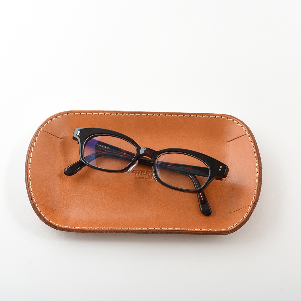 職人手作皮革小物收納盤，皮革材質，咖啡色，表面有細緻車縫線，盤上放置一副黑框眼鏡。