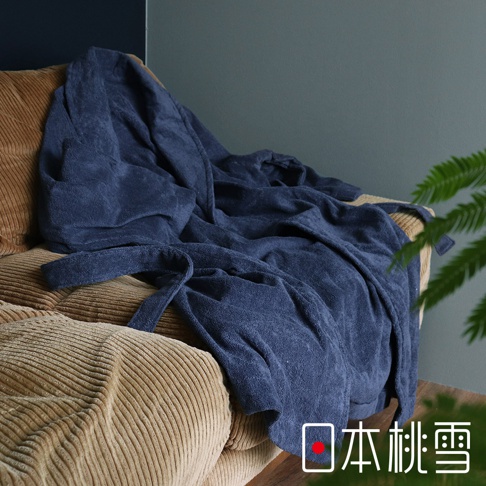 深藍色長袖連帽浴袍，採用柔軟的純棉材質，腰間繫有同色系腰帶，搭配卡其色燈芯絨沙發，背景為灰綠色牆面與綠色植物。