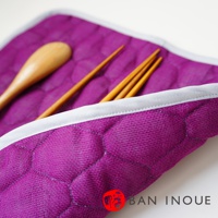 一個紫色的棉織吸水墊，表面有菱格紋縫線，置入一把木製湯匙和三根木筷。