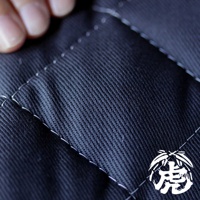 深藍色竹炭床墊表面，布料紋理清晰，白色縫線勾勒出菱形格紋。左上角可見一隻手指。右下角有白色「虎」字樣的品牌標誌。