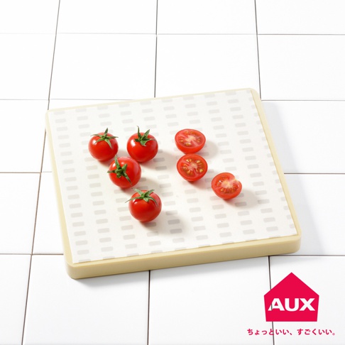 白色格紋防汙紙覆蓋在淺黃色砧板上，上方擺放著三顆完整的小番茄和三顆對半切開的小番茄，皆為鮮紅色。