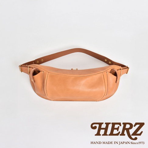 HERZ 職人手作皮革大容量斜背包 F-1，淺棕色牛皮材質，簡約設計，附有可調整式肩背帶，背面有HERZ品牌標誌。