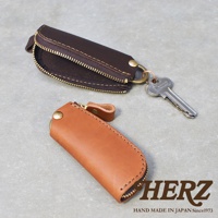 職人手作皮革Organ拉鍊鑰匙包，展示深棕色和淺棕色兩款。深棕色鑰匙包拉鍊部分打開，露出內部，並掛有一把鑰匙。淺棕色鑰匙包閉合，呈現簡潔的造型。兩款鑰匙包均採用皮革材質，配有金色拉鍊和金屬扣。