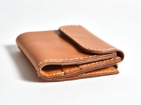 職人手作的方形短夾，採用光滑的淺棕色皮革製成，搭配米白色縫線，展現簡約質感。短夾設計緊湊，可見層疊的皮革結構。