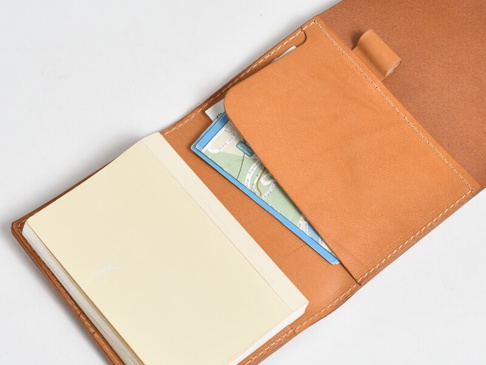 職人手作皮革A6記事本書套，淺棕色皮革，內含一本淺黃色封面的記事本及一張藍色地圖卡片，縫線整齊。