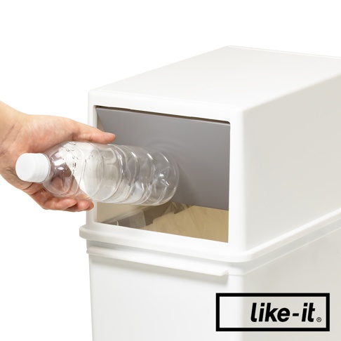 一只手正將一個透明塑膠瓶放入白色垃圾桶的灰色推蓋開口。