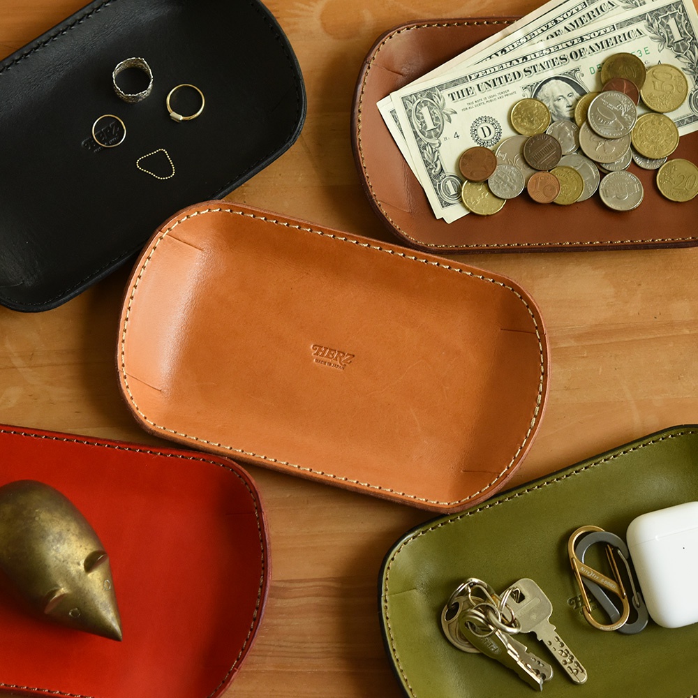 職人手作皮革小物收納盤，共展示四色：黑色、棕色、紅色、綠色。盤內分別收納戒指、硬幣、紙鈔、鑰匙及無線藍牙耳機。